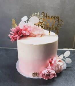 Gâteau d'anniversaire rose ombré avec dessus "Happy Birthday" doré, décoré de fleurs roses et de feuilles dorées, portant le chiffre "60".