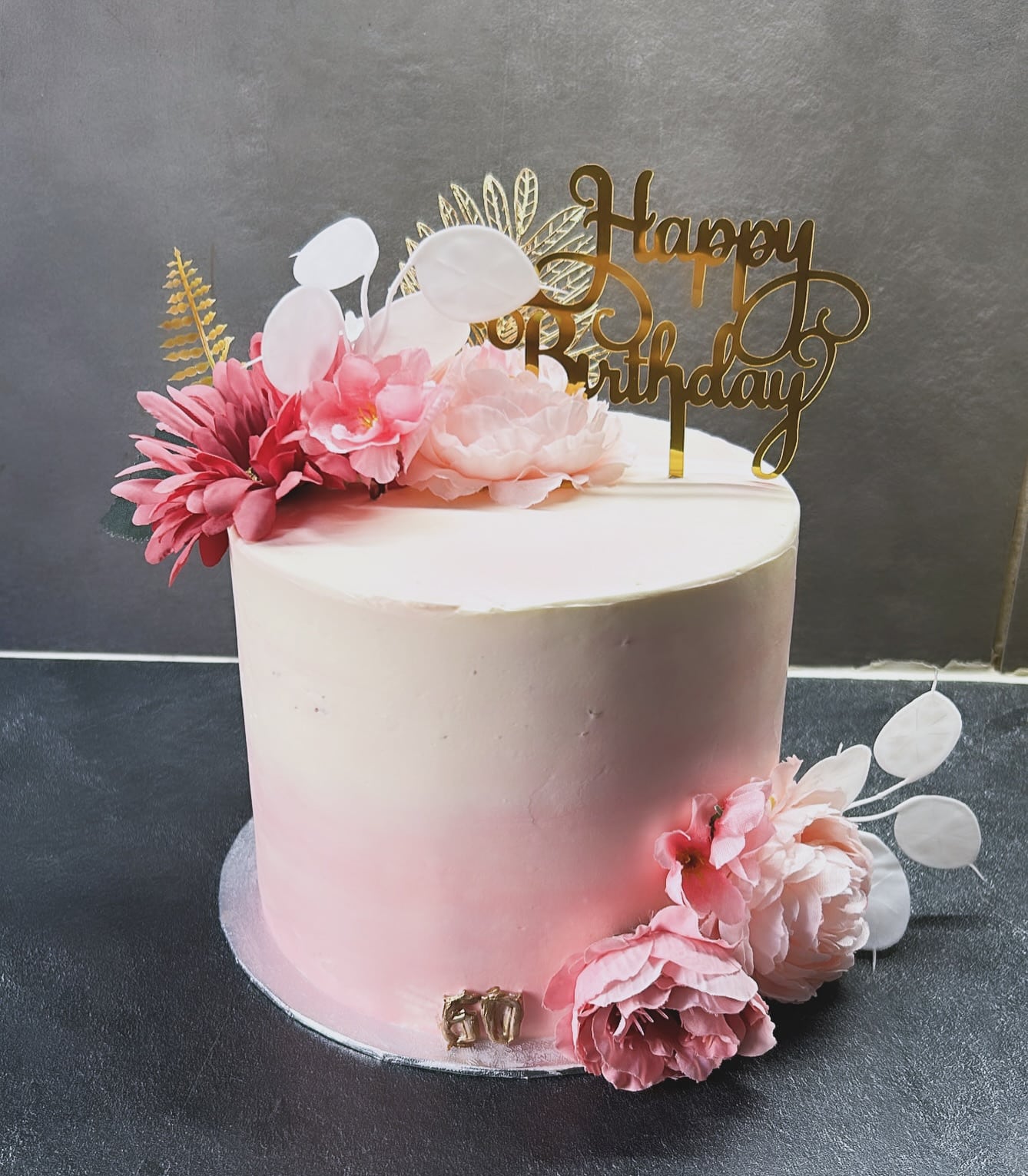 Gâteau d'anniversaire rose ombré avec dessus "Happy Birthday" doré, décoré de fleurs roses et de feuilles dorées, portant le chiffre "60".