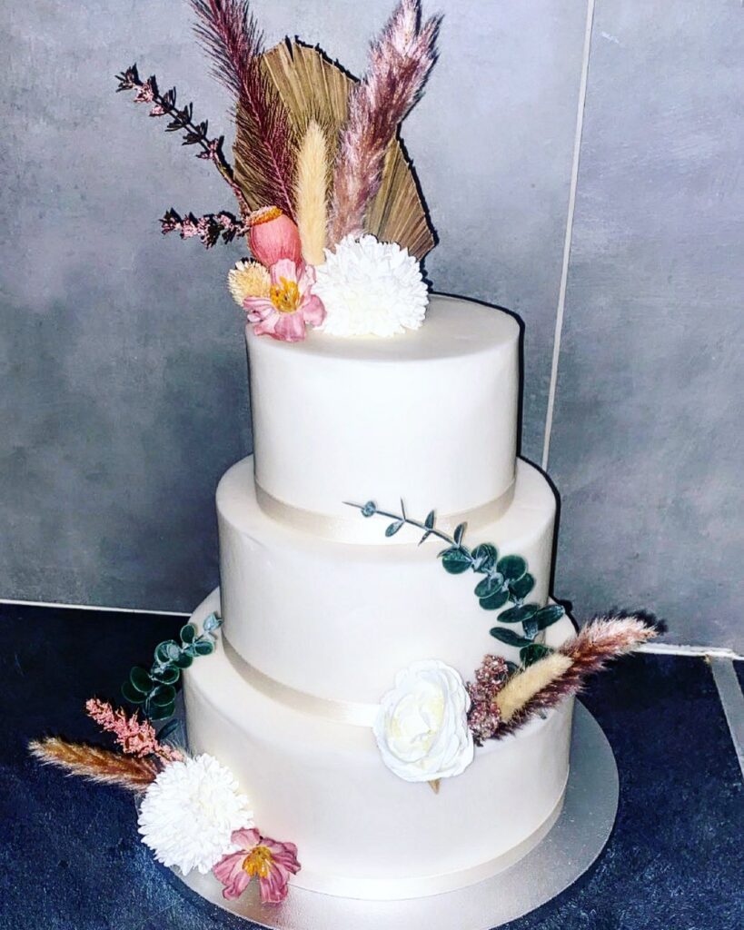 Gâteau Mariage Bohème Chic Fleurs Séchées Trois Étages Gâteau de mariage blanc trois étages décoré de fleurs séchées, de graminées pampas et de feuillage eucalyptus dans un style bohème chic.