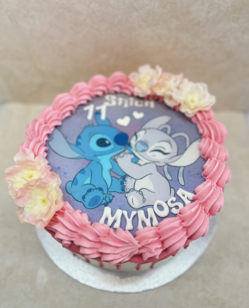 Gâteau Stitch (bleu) et Angel (gris-rose) s'embrassant, bordure rose, fleurs pâles. Inscription '11 Stitch MYMOSA'.