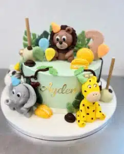Gâteau d'anniversaire jungle pour Ayden, décoré de figurines en pâte à sucre : lion, éléphant, girafe, macarons jaunes et feuillage tropical.