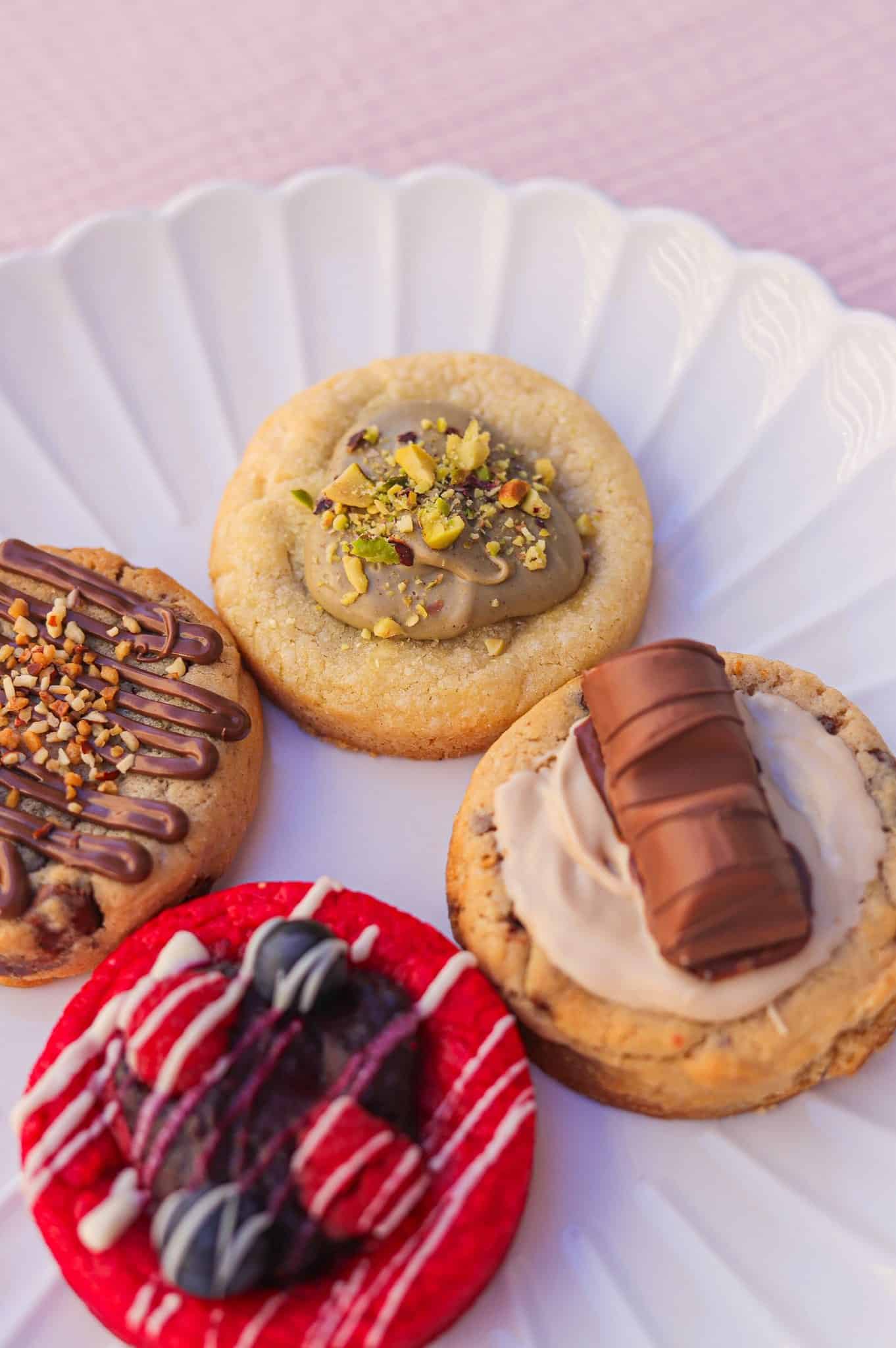 Assortiment de cookies gourmands : pistache, chocolat, Kinder et fruits rouges sur une assiette blanche.