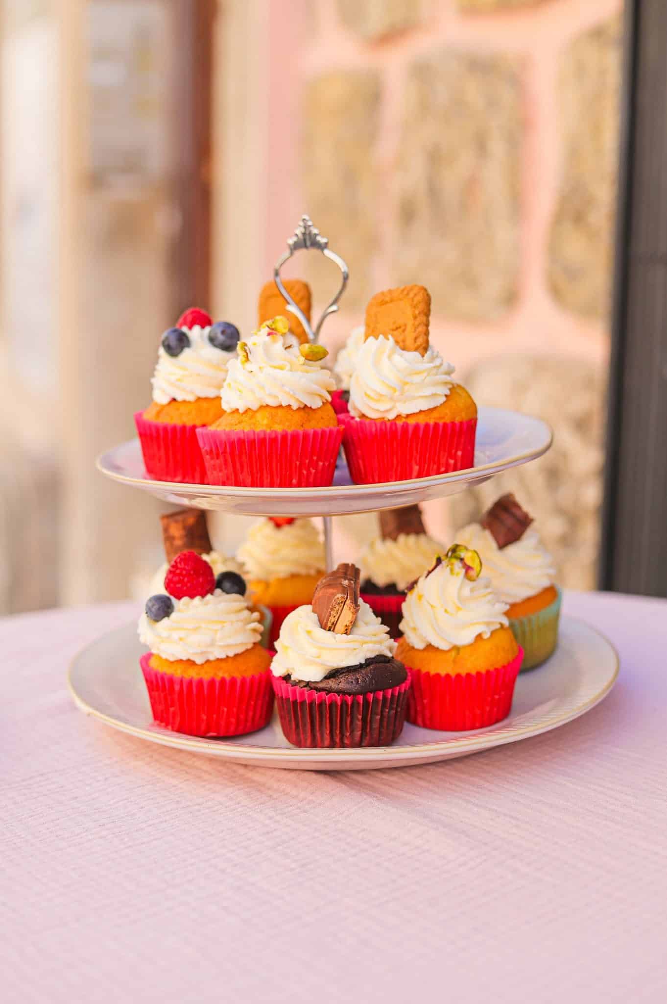 Plateau de cupcakes gourmands décorés de fruits et chocolat sur un présentoir à deux étages festif.