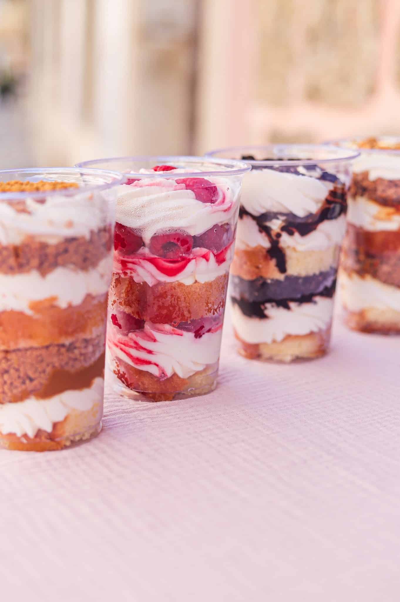 Verrines de desserts gourmands aux couches de framboise, chocolat et biscuit sur une nappe rose.